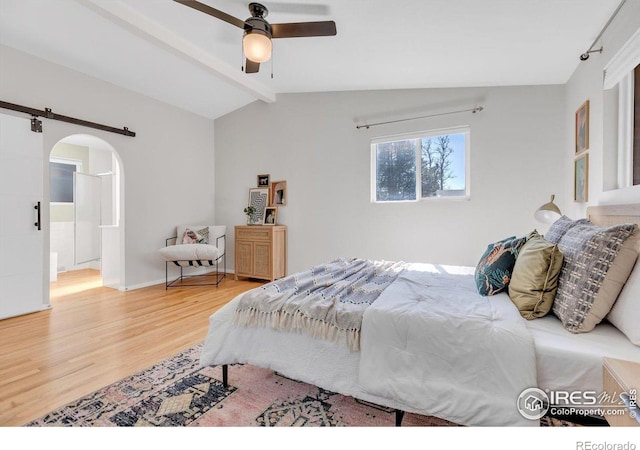 bedroom with arched walkways, vaulted ceiling with beams, a barn door, a ceiling fan, and wood finished floors