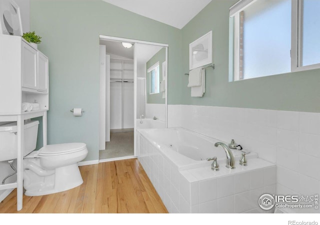 bathroom with toilet, a tub with jets, and wood finished floors