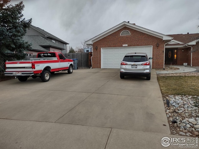 exterior space with driveway, brick siding, an attached garage, and fence