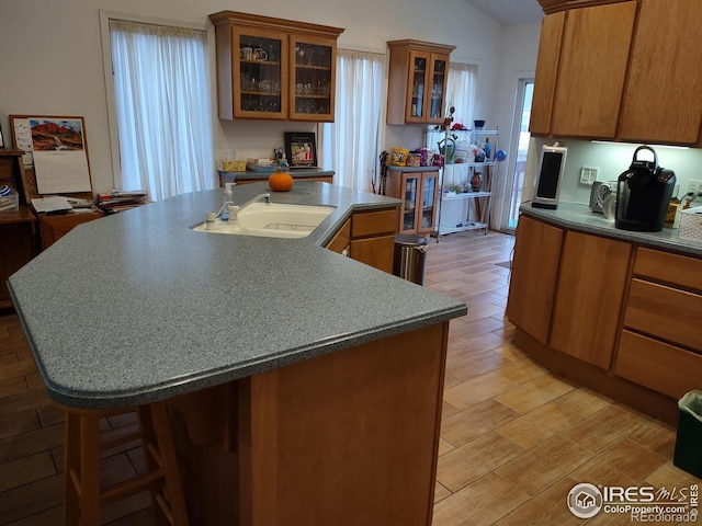 kitchen with light wood-type flooring, a center island with sink, brown cabinets, lofted ceiling, and a sink