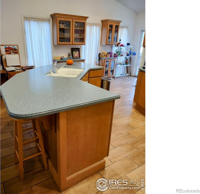 kitchen featuring vaulted ceiling, a large island, glass insert cabinets, brown cabinets, and a sink