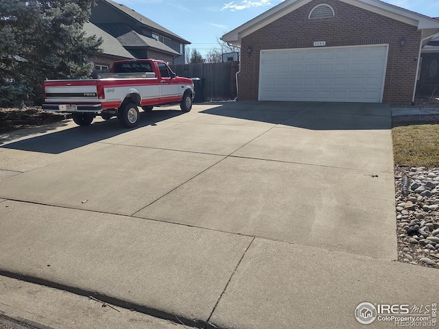 view of property exterior featuring concrete driveway, brick siding, an outdoor structure, and fence