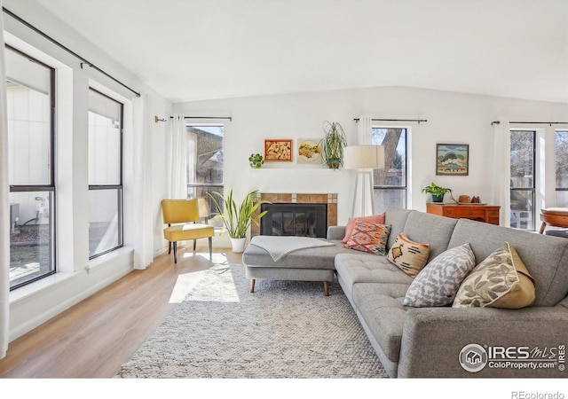 living room featuring light wood-type flooring, baseboards, lofted ceiling, and a tile fireplace