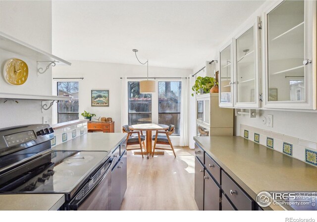 kitchen with decorative light fixtures, light countertops, electric range oven, glass insert cabinets, and light wood-type flooring