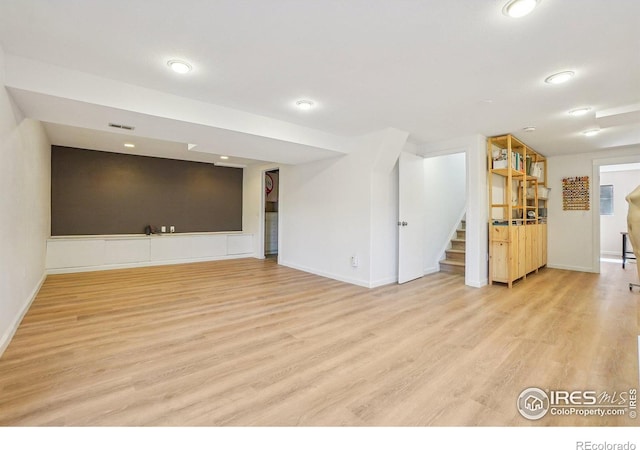 unfurnished living room with baseboards, visible vents, stairway, and light wood finished floors