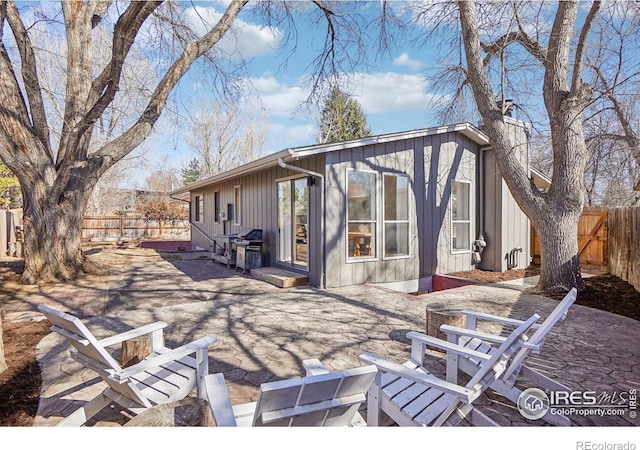 back of house with board and batten siding, a fenced backyard, a patio, and a chimney