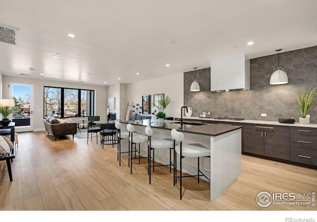 kitchen with tasteful backsplash, visible vents, light wood-style flooring, a sink, and a kitchen breakfast bar