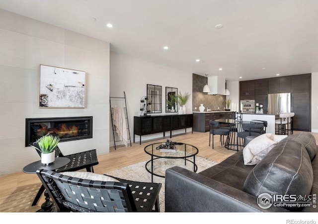 living room featuring light wood-type flooring, recessed lighting, and a glass covered fireplace