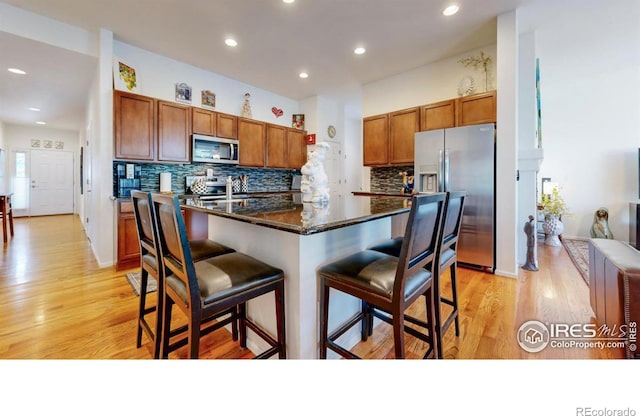 kitchen with stainless steel appliances, brown cabinetry, light wood-style flooring, and a kitchen breakfast bar