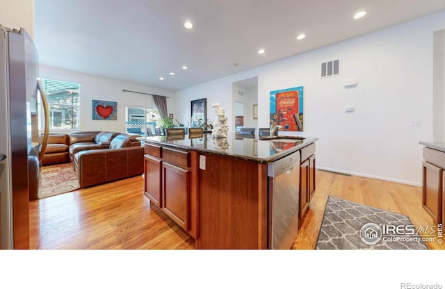 kitchen with light wood finished floors, stainless steel appliances, visible vents, open floor plan, and an island with sink