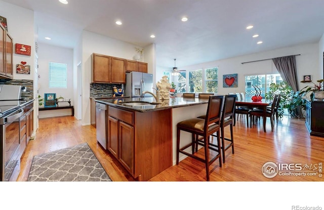 kitchen with backsplash, light wood-style flooring, appliances with stainless steel finishes, brown cabinetry, and a sink