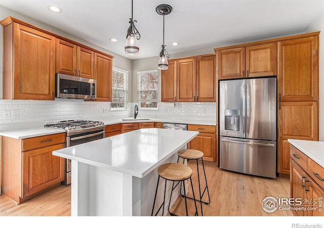 kitchen with brown cabinetry, appliances with stainless steel finishes, a breakfast bar area, light countertops, and light wood-type flooring