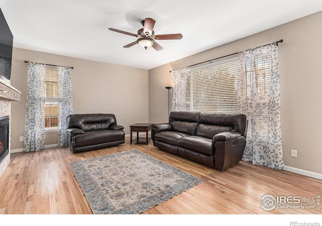 living room with a ceiling fan, a glass covered fireplace, baseboards, and wood finished floors