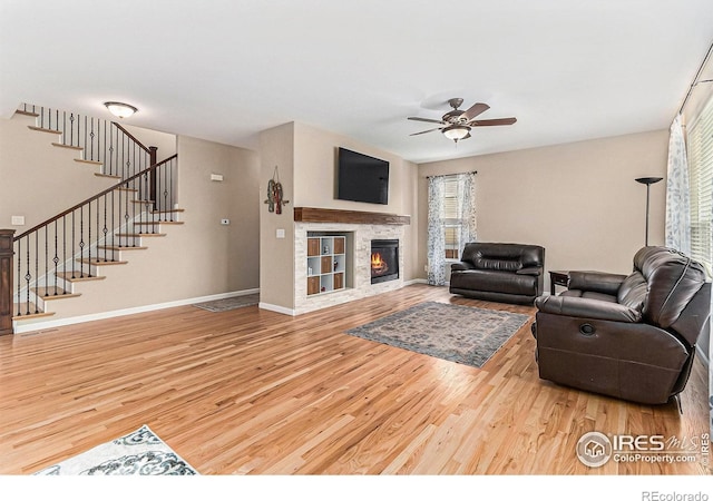 living room featuring baseboards, a glass covered fireplace, ceiling fan, wood finished floors, and stairs