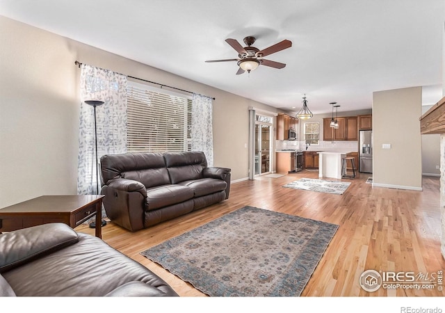 living area with light wood-style flooring, baseboards, and a ceiling fan