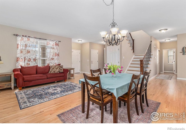 dining area featuring light wood finished floors, plenty of natural light, stairway, and an inviting chandelier