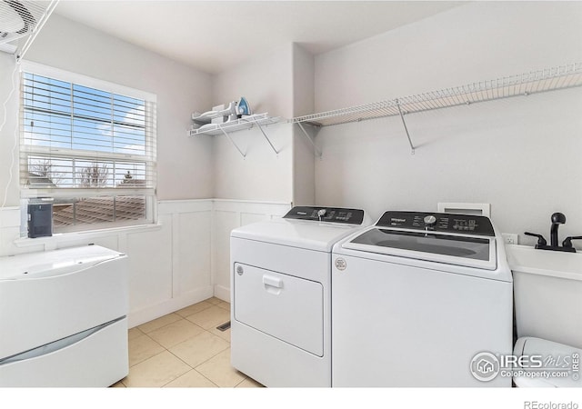 laundry room with washing machine and clothes dryer, wainscoting, a sink, light tile patterned flooring, and laundry area