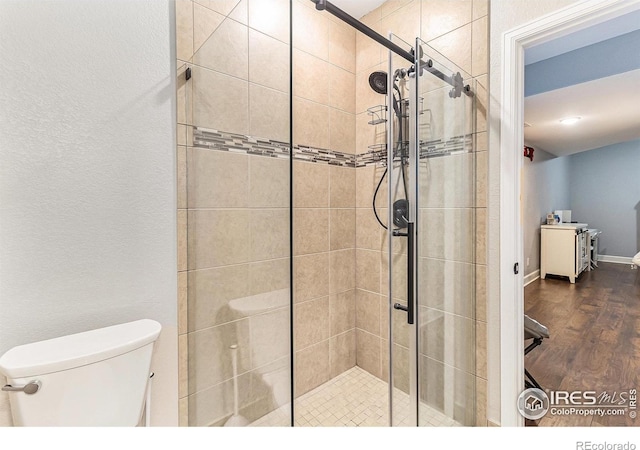 full bath featuring toilet, a shower stall, baseboards, and wood finished floors