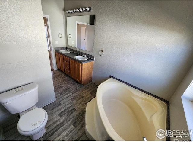 full bathroom featuring a garden tub, toilet, wood finished floors, a sink, and double vanity