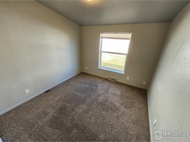 spare room with carpet floors, visible vents, a textured wall, and baseboards