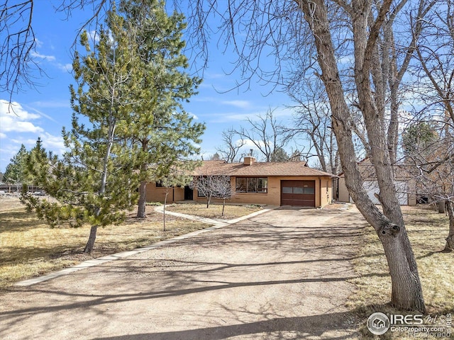 view of front of house with an attached garage, dirt driveway, a chimney, and brick siding