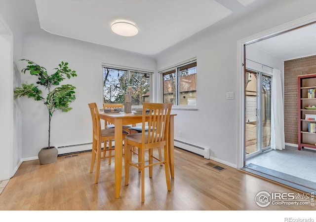 dining space featuring light wood finished floors, a baseboard radiator, visible vents, and baseboards