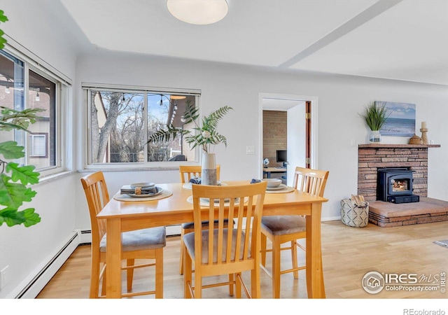 dining room with a baseboard heating unit, a wood stove, and wood finished floors