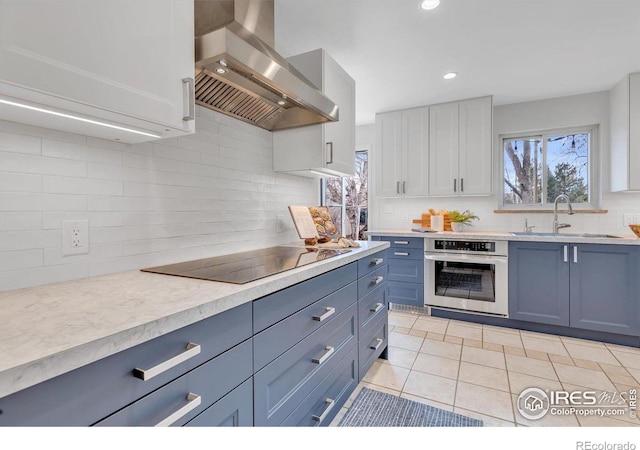 kitchen with oven, black electric cooktop, light countertops, ventilation hood, and a sink