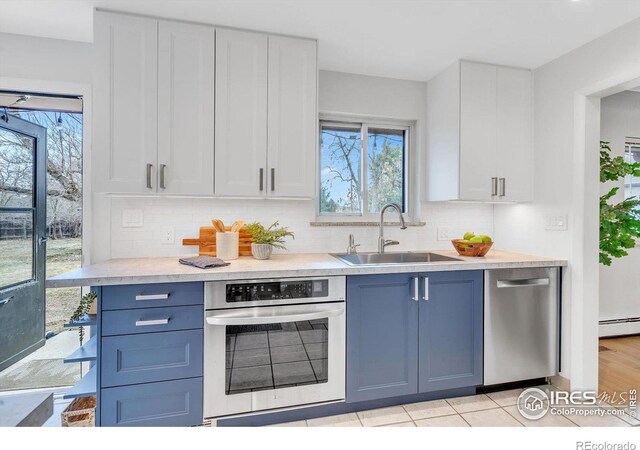 kitchen with stainless steel appliances, a baseboard radiator, white cabinetry, and a sink