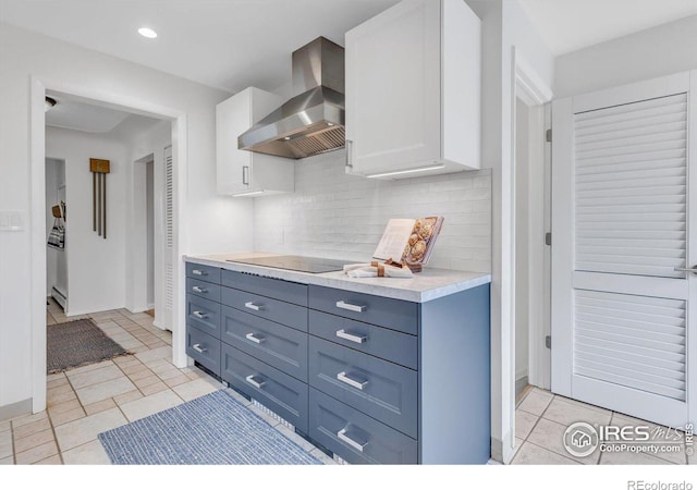 kitchen with light countertops, white cabinets, wall chimney range hood, and decorative backsplash