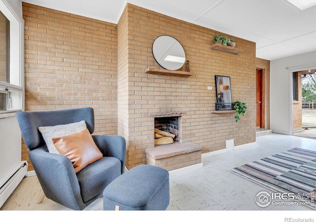 living area with a baseboard heating unit, brick wall, and an outdoor brick fireplace