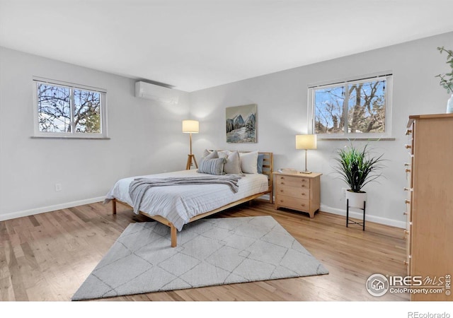 bedroom with a wall mounted AC, baseboards, and wood finished floors