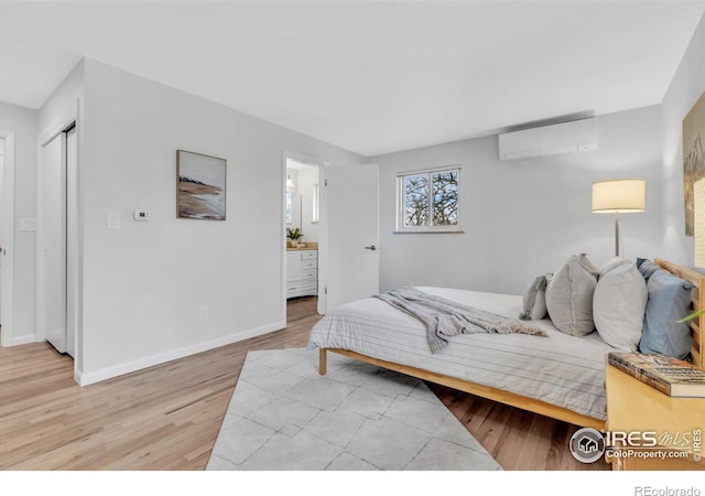 bedroom featuring ensuite bath, light wood-style flooring, baseboards, and a wall mounted AC