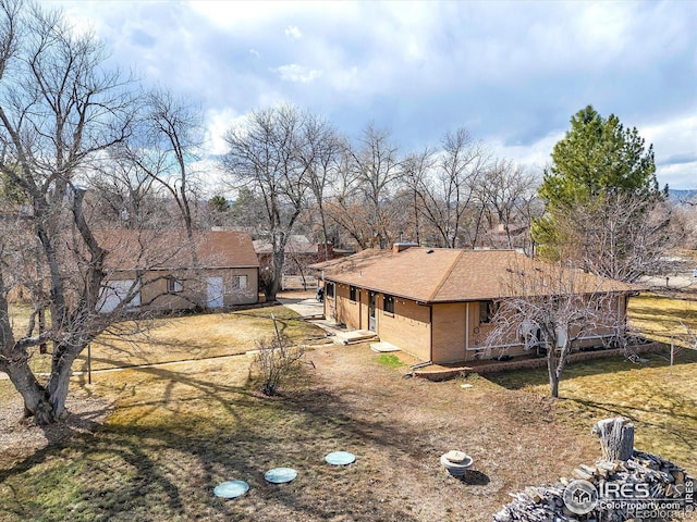 view of front of house with roof with shingles, dirt driveway, and brick siding