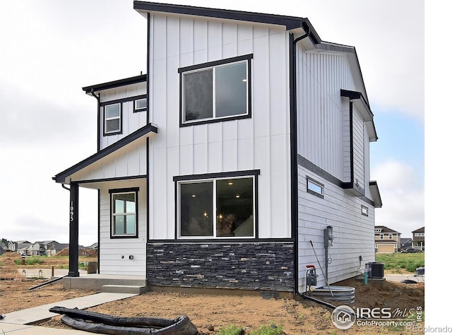 rear view of house featuring stone siding, central AC unit, and board and batten siding