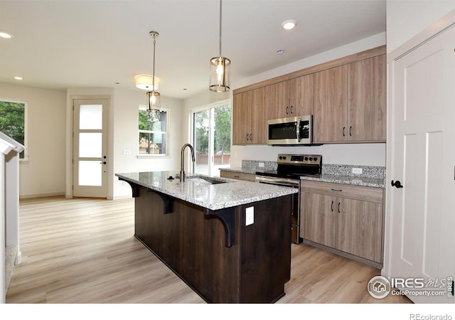 kitchen with a sink, light wood-style floors, appliances with stainless steel finishes, a kitchen bar, and a center island with sink