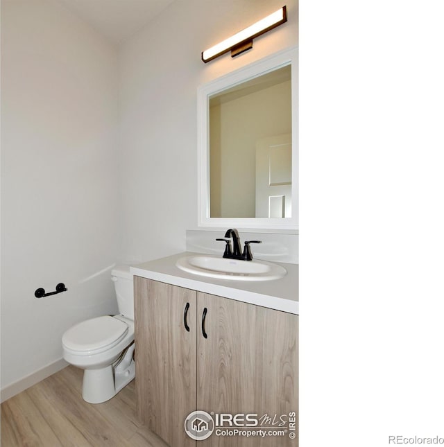 half bath featuring vanity, toilet, and wood finished floors