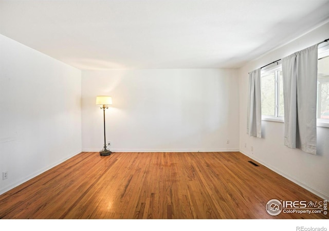 empty room featuring visible vents, baseboards, and wood finished floors