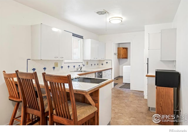 kitchen featuring tasteful backsplash, white cabinets, a breakfast bar, a peninsula, and a sink