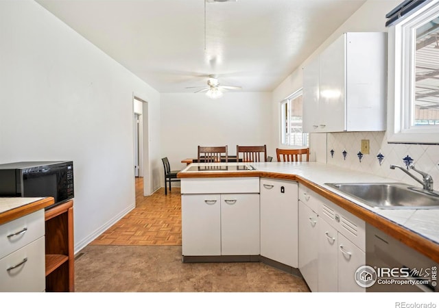 kitchen featuring tasteful backsplash, white cabinets, a peninsula, black microwave, and a sink