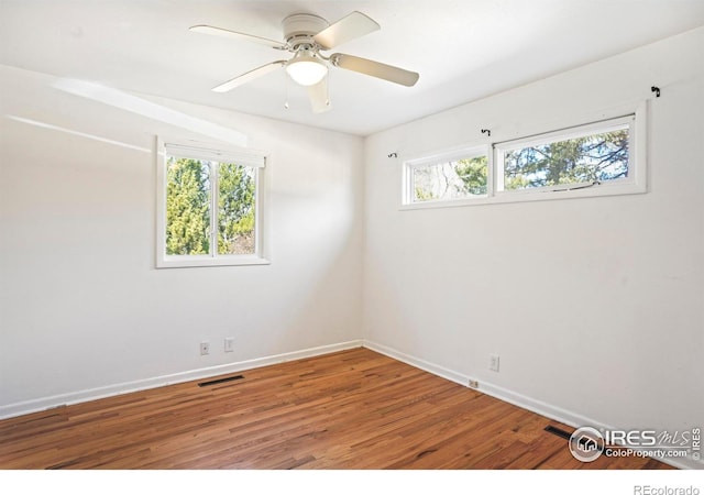 empty room with plenty of natural light, visible vents, baseboards, and wood finished floors