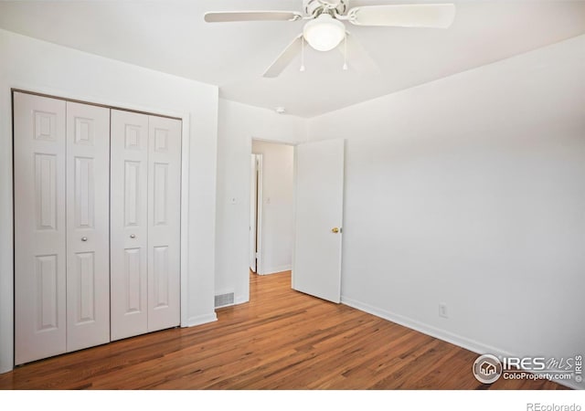 unfurnished bedroom with baseboards, visible vents, ceiling fan, wood finished floors, and a closet