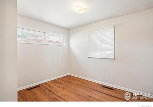 empty room with baseboards, visible vents, and wood finished floors