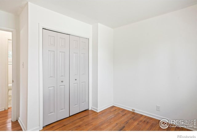 unfurnished bedroom featuring light wood-style floors, baseboards, and a closet