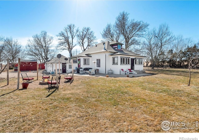 rear view of house featuring stucco siding, an outdoor fire pit, a patio, and a yard