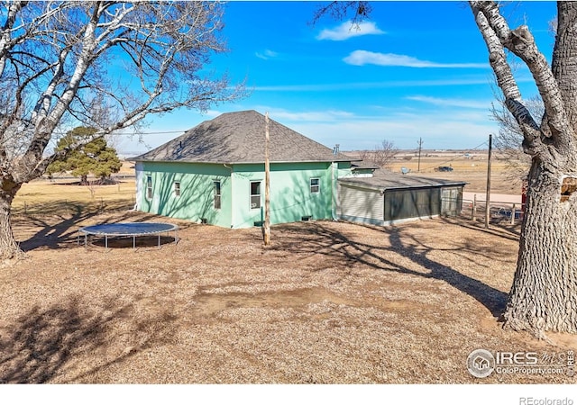 rear view of property featuring a trampoline, stucco siding, a shingled roof, fence, and an outdoor structure