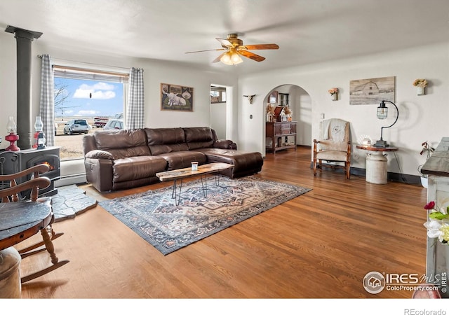 living area with arched walkways, ceiling fan, wood finished floors, and a wood stove