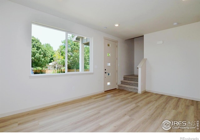 empty room featuring recessed lighting, wood finished floors, baseboards, and stairs