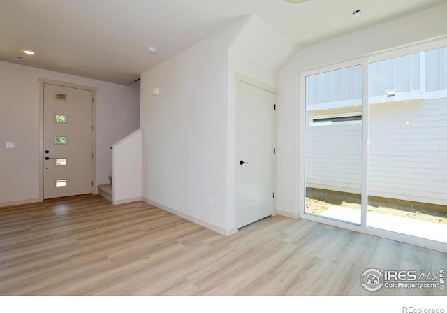 unfurnished room featuring stairway, light wood-style flooring, and baseboards