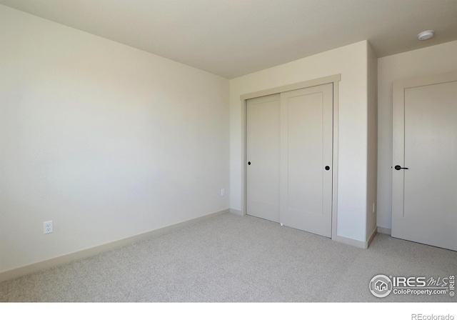 unfurnished bedroom featuring baseboards, a closet, and light colored carpet